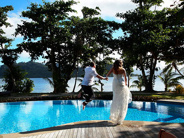 A loving couple smiling and embracing in an infinity pool with a stunning ocean backdrop. The serene setting includes palm trees and an expansive sky, perfect for a romantic getaway.