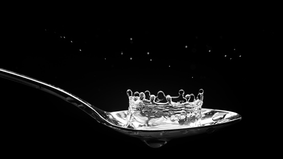A water splash on a spoon has formed a crown shape.  Wet spoon with droplets flying.  Black background