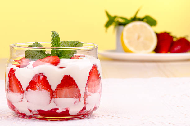 Strawberries desert with cream served on glass cups over table top.