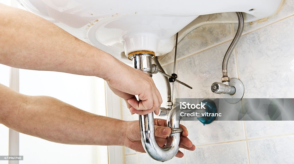 Plumber at work Plumber using a wrench to tighten a siphon under a sink 2015 Stock Photo