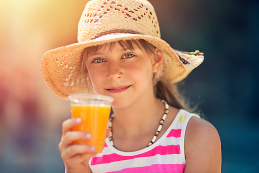 Portrait of a little tourist girl drinking a glass of fresh orange juice. The girl is aged 8 and is holding a plastic cup of fresh orange juice. Spain, Mallorca.