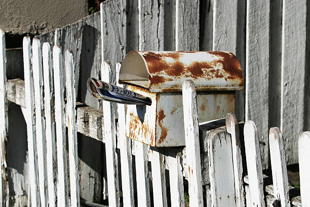 Rusty letterbox on a white picket fence Rusty white metallic letterbox on a white picket fence, with a newspaper poking out rusty fence stock pictures, royalty-free photos & images
