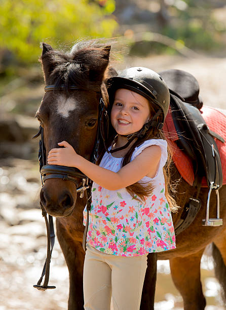 little girl with little pony horse happy in jockey helmet sweet beautiful young girl 7 or 8 years old hugging head of little pony horse smiling happy wearing safety jockey helmet posing outdoors on countryside in summer holiday pony photos stock pictures, royalty-free photos & images
