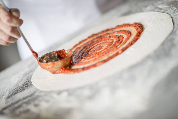 Close up of a man making pizza at an italian restaurant and putting sauce on the dough