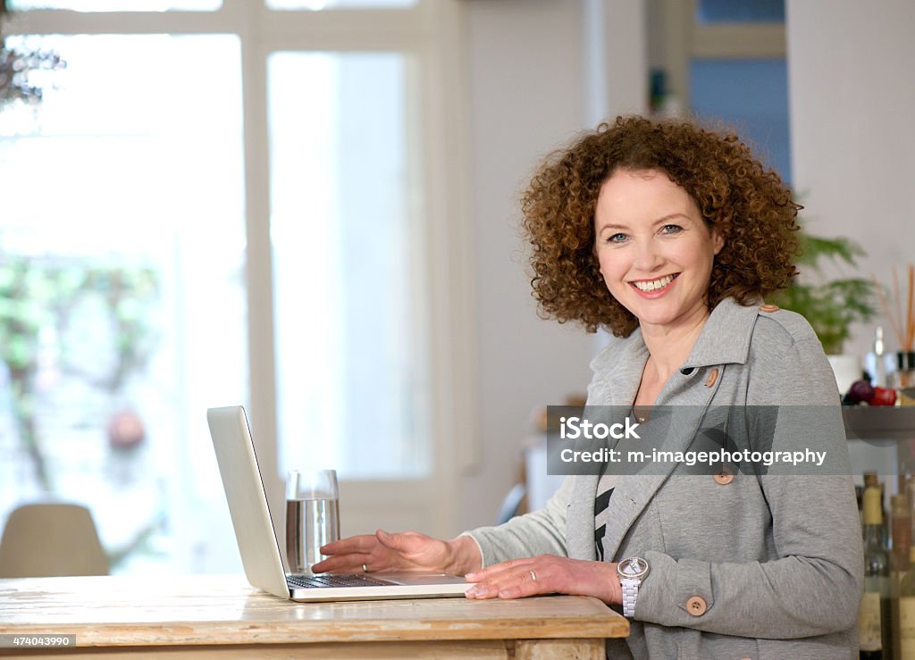 Happy woman using laptop at home Portrait of a happy middle aged woman using laptop at home 2015 Stock Photo
