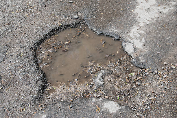 istock damage to tarmac road with potholes and puddles 474048524