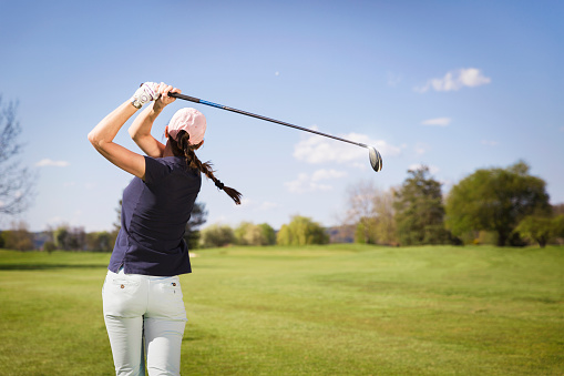 Female golf player swinging golf club.