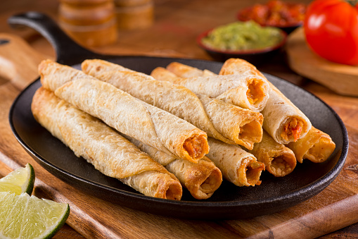 A platter of delicious chicken taquitos with salsa, guacamole, and lime.
