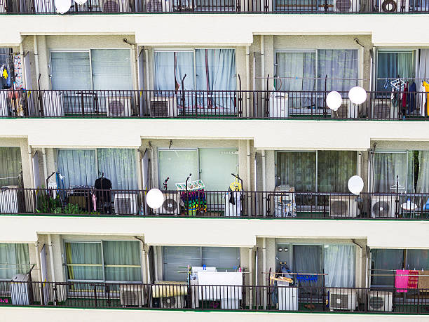 Common facade of a building with many balconies of an apartment building. Each balcony has air conditioning device, washing machine and something for air drying. This is near Shinjuku centre in Tokyo, Japan.