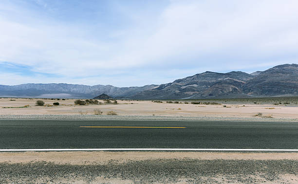 istock Road in Mojave desert with cloudy sky and striped mountains 474062772