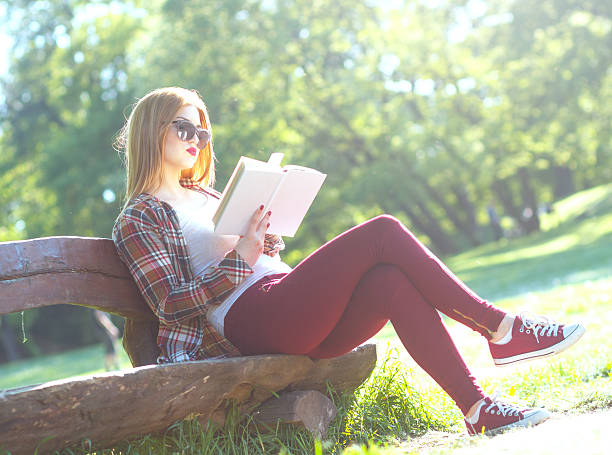 istock Young woman sitting in the park and reading book 474073630