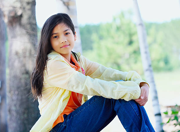 istock Young biracial girl sitting on rock under trees 474075105