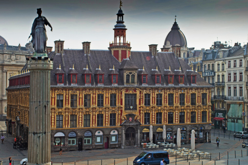 Lille, United Kingdom - August 28, 2013: Panorama of Lille Grand Palais with some tourists in the foreground. There are cobered seating areas outside the restaurants and cars travelling at the bottom of the shot.
