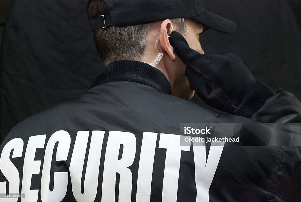 Security Guard Listens To Earpiece, Back of Jacket Showing Close-up of a security guard listening to his earpiece. Back of jacket showing. Security Staff Stock Photo