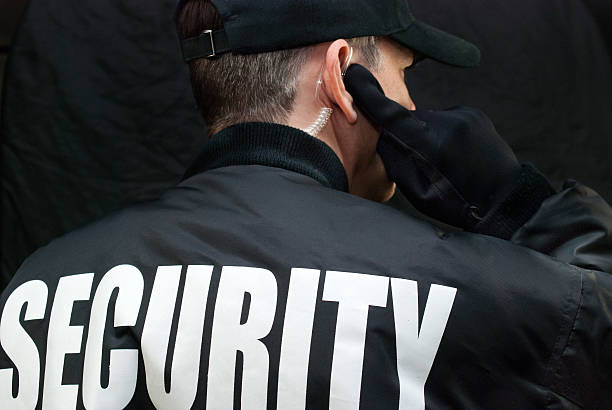 Security Guard Listens To Earpiece, Back of Jacket Showing Close-up of a security guard listening to his earpiece. Back of jacket showing. security guard photos stock pictures, royalty-free photos & images