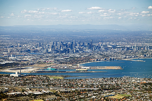 Aerial view of Melbourne city, port and surrounding suburbs – panoramic view from light aircraft.  Shows Webb Dock Yarra River, Newport Power Station, Newport Railway Workshops, Bolte Bridge, Rialto building, Melbourne Eye, MCG, sporting stadiums, freeways.  Horizontal, suitable for crop to panorama format, some vibration movement.