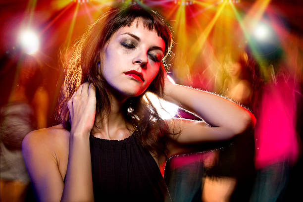 Drunk or High at a Nightclub Disheveled drunk female with ruined make up in a nightclub.  She is drunk or high on drugs.  The people in the background are partying and dancing and motion blurred.  The woman looks like an outcast and is self destructive by abusing drugs or alcohol.  self destructive stock pictures, royalty-free photos & images