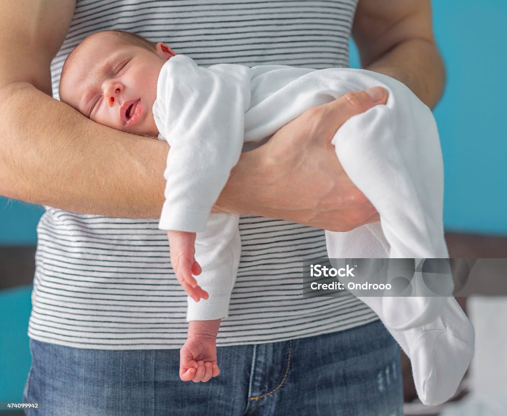 A one month old baby is asleep in an arm of a standing man Monthly baby sleeping on the arm of his father's hand, position to help colic Baby - Human Age Stock Photo