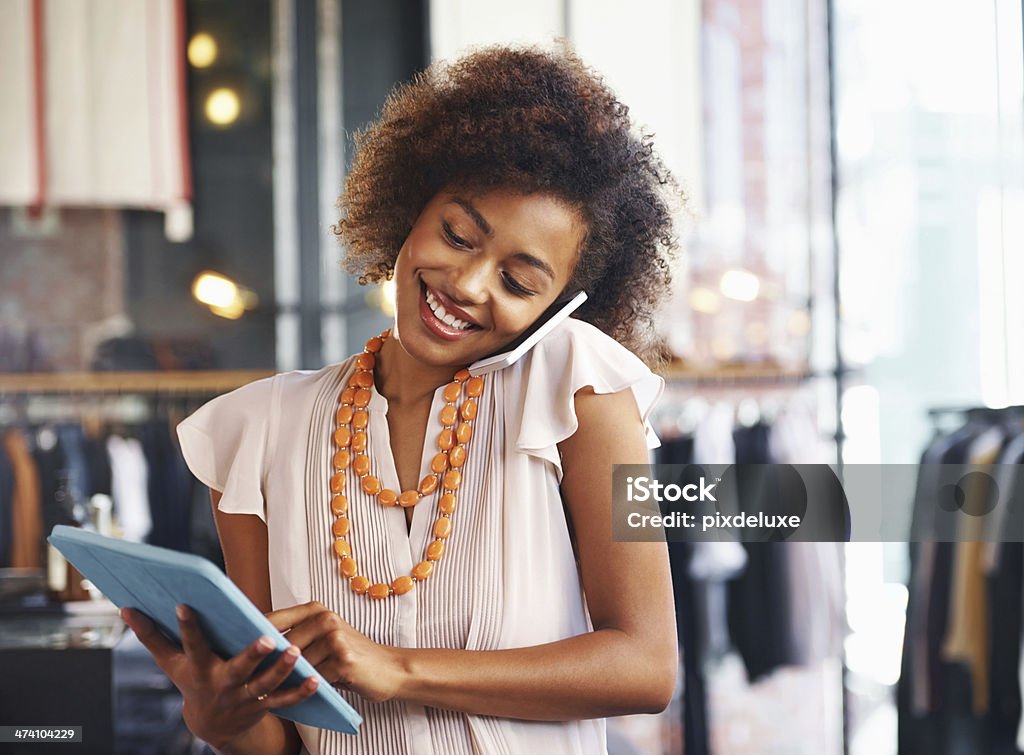 Woman using a digital tablet and talking on phone Shot of a woman holding a digital tablet and talking on her phone in her clothing boutique Shopping Mall Stock Photo