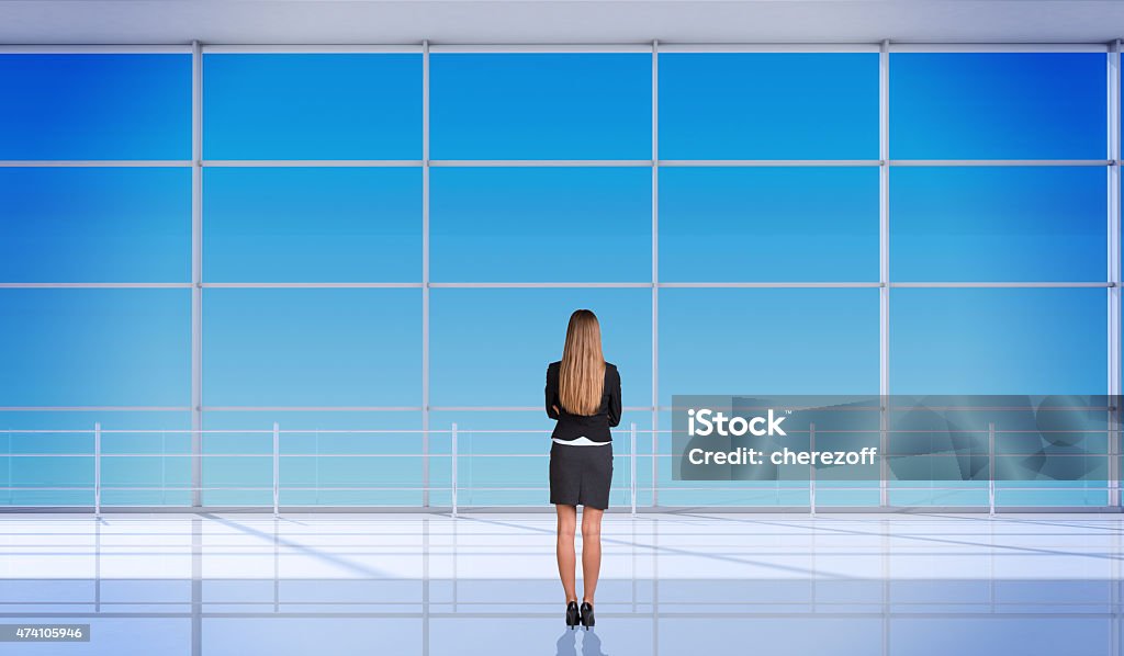 Young businesslady with crossed arms Young businesslady with crossed arms and standing back in front of window. Interior view 2015 Stock Photo