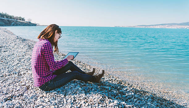istock Girl sitting with digital tablet on beach 474109160