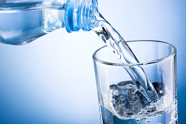 primer plano de verter agua de botella en vidrio sobre fondo azul - agua purificada fotografías e imágenes de stock