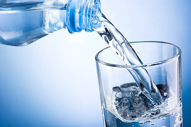 close-up de água vertendo do frasco em vidro em fundo azul - water water bottle glass pouring imagens e fotografias de stock