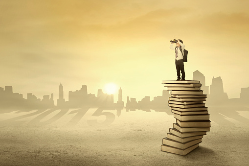 Little boy standing on books and use a telescope for looking his vision in 2015