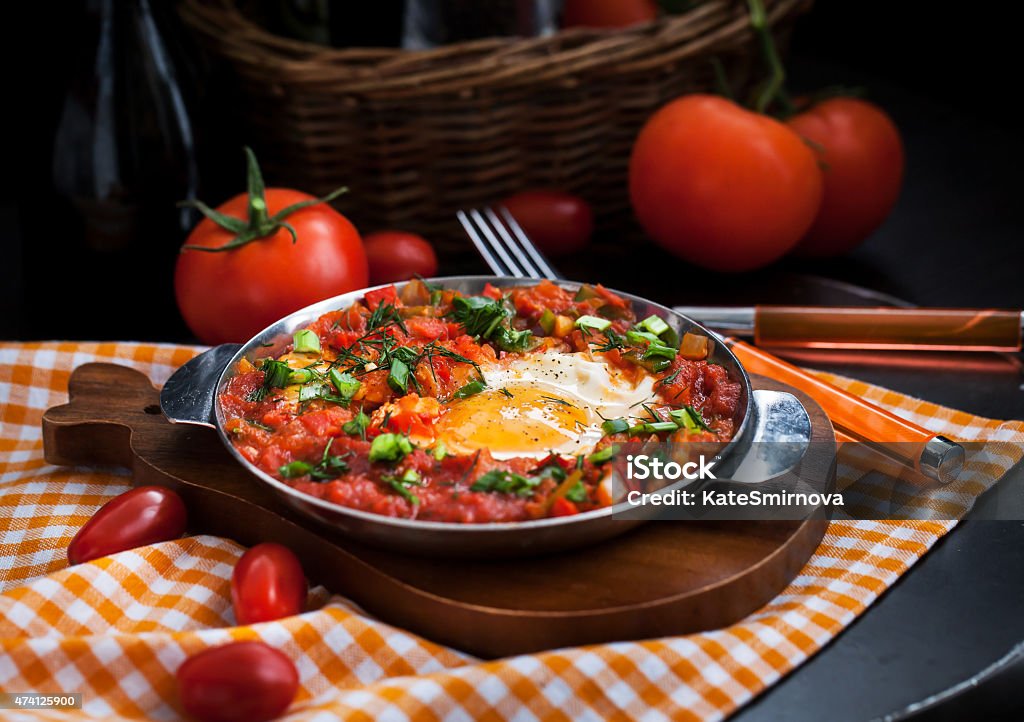 Shakshuka with tomatoes and eggs Shakshuka - fried eggs with tomatoes, onion, pepper and spices in iron pan, dark style Kitchen Stock Photo