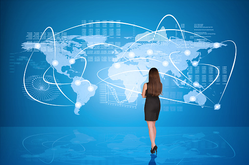 Businesswoman in black dress with crossed arms in front of holographic screen, back view. Earth land map derived from public NASA observatory - http://visibleearth.nasa.gov/view_rec.php?id=2433