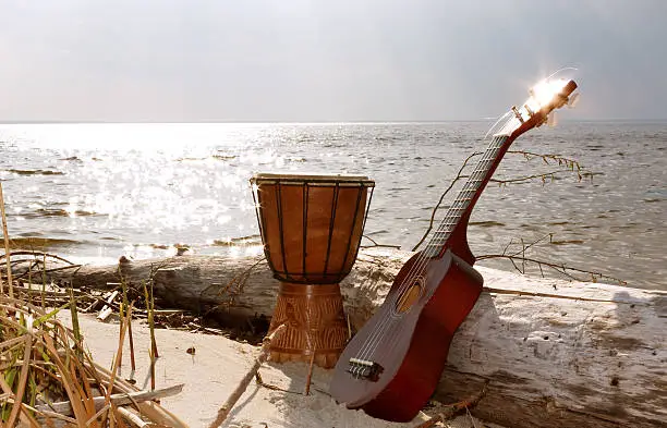 Ukulele & ethnic drum on a beach on a sea and sky background.