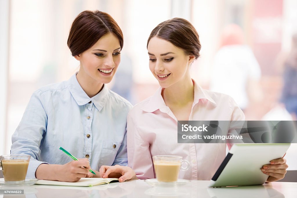 Bisinesswomen with tablet Two young beautiful businesswomen  sitting in urban cafe and using digital tablet. 2015 Stock Photo