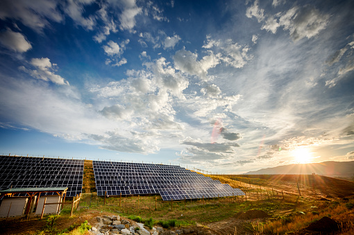 HDR image of a row of solar panels at sunset under a beautiful cloudscape with lens flares and sun rays