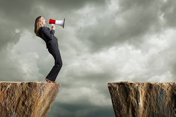 деловая женщина, стоя на скале кричать в рупор - cliff finance risk uncertainty стоковые фото и изображения