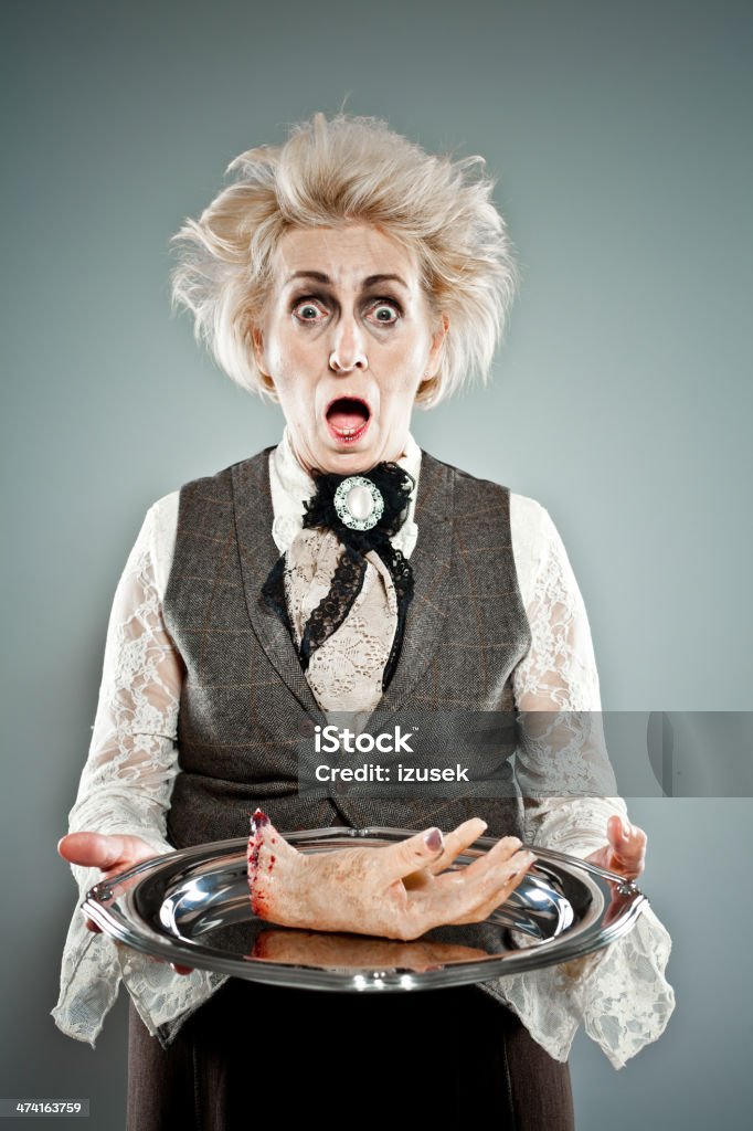 Spooky senior lady Contemporary portrait of victorian style spooky countess serving a human hand on the tray. Studio shot. Halloween Stock Photo
