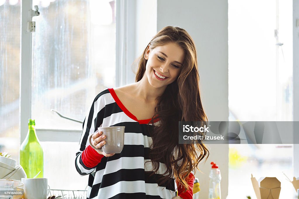 Morning coffee Smiling beautiful young woman standing in the kitchen with a cup of coffee. Coffee - Drink Stock Photo