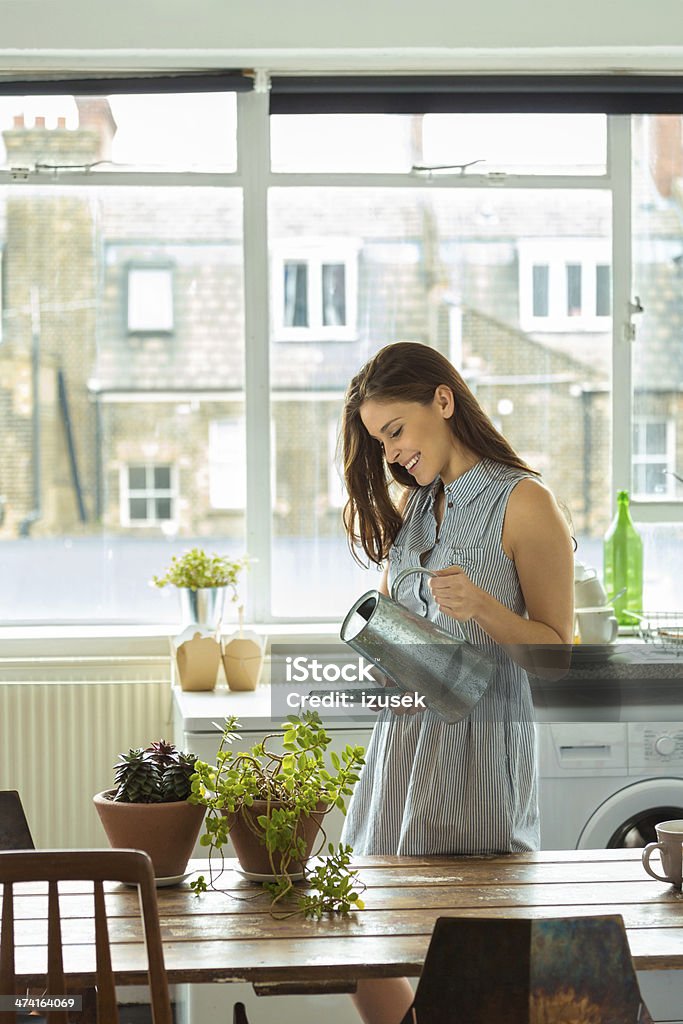 Woman watering plants Smiling young woman watering plants in her home. Watering Stock Photo
