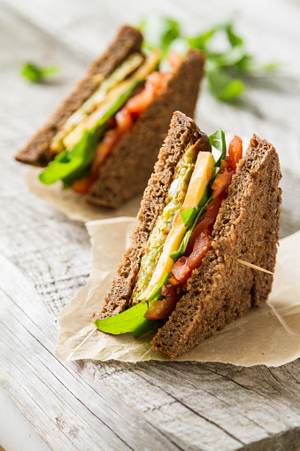 Vegetable sandwich with zucchini burger, cheese, ruccola and tomatoes, baking paper, rustic wood background