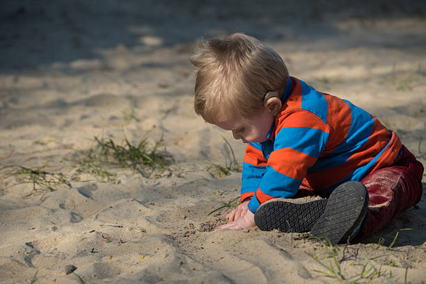 istock Baby boy with hearing aid digging in sand 474171308