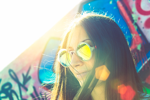 Portrait of hipster young woman with sun flare effect, graffiti on background.