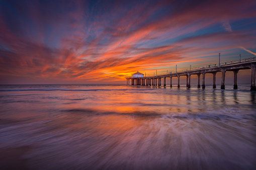 A pier sits on the ocean while the sun sets with absolutely stunning clouds in the sky.