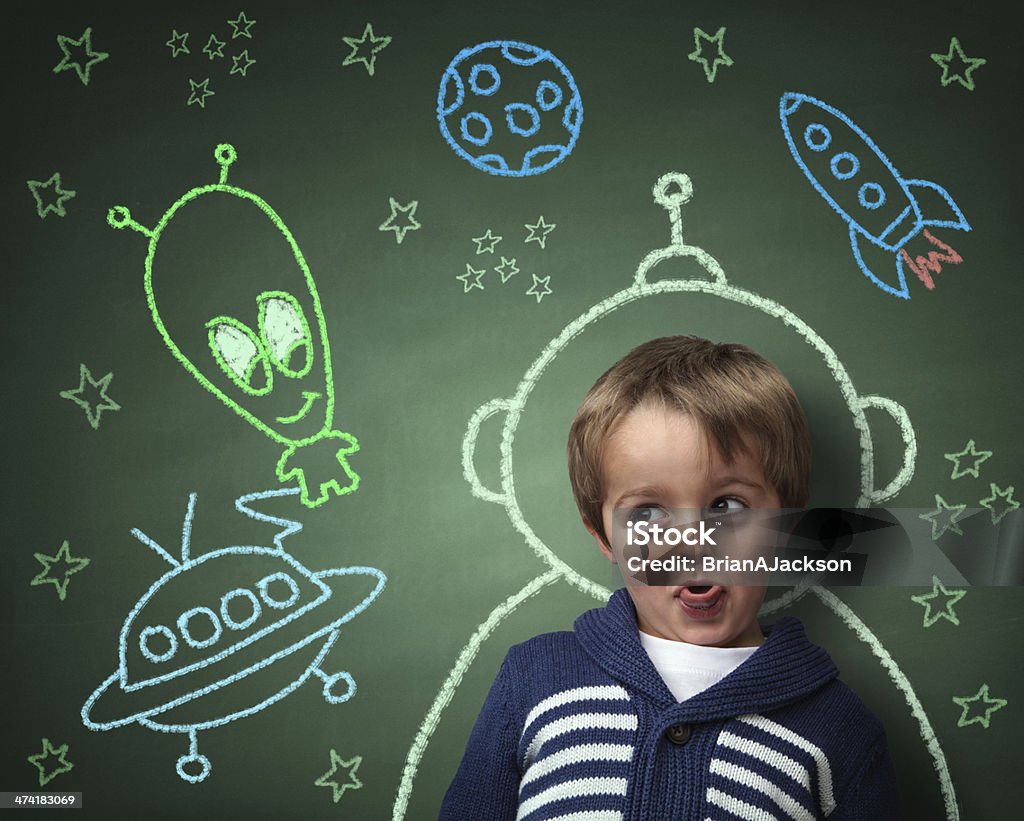 Childhood imagination and dreams Imagination and dreams of a child, dressed as a space man in front of a blackboard with chalk drawings of space rocket and alien, concept for aspirations and daydreaming Child Stock Photo