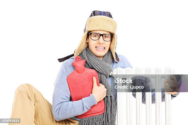 Chilled Young Man With Hot Water Bottle Hugging A Radiator Stock Photo - Download Image Now