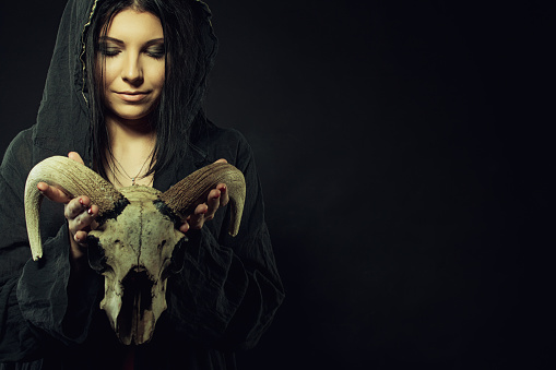 Pretty young girl in hood holding skull over dark background