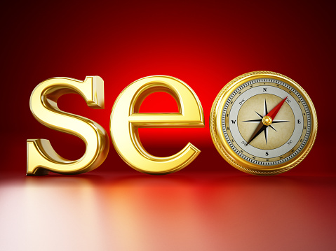 Gold SEO text (Search Engine Optimization) with a compass standing on red reflective background.