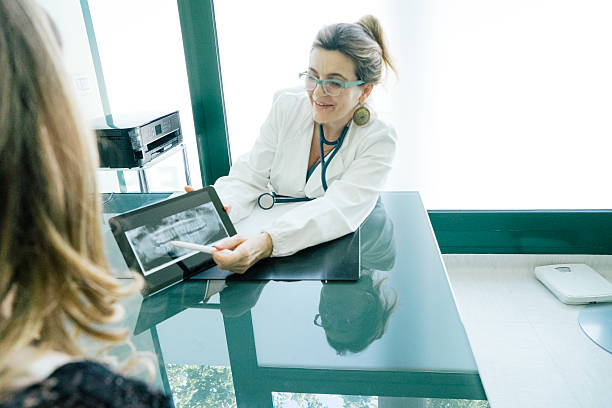 joyeuse femme médecin expliquant x-ray image pour patient - doctor digital display digital tablet healthcare and medicine photos et images de collection