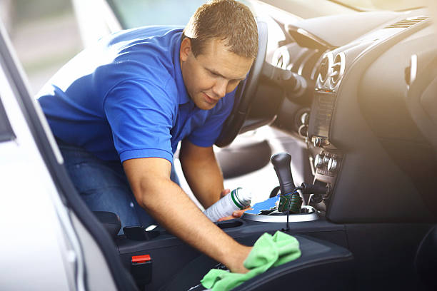 Man cleaning upholstery of his vehicle. Adult caucasian man cleaning passenger seat with a green cloth and cleaning product. He applied some cleaning foam onto the seat. The guy has short brown hair and wearing blue polo shirt. car for sale stock pictures, royalty-free photos & images
