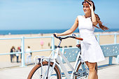 woman dressed in white  holding white bike enjoying sun near sea
