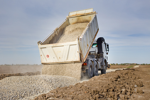 Tipping truck unloading gravel on road construction site