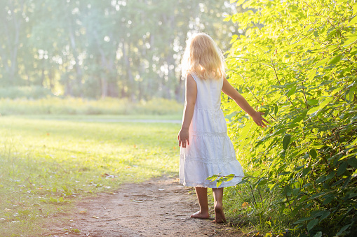 A little blonde girl wearing a white dress standing barefoot on a path